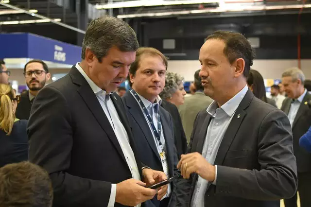 Governador Eduardo Riedel conversa com Walter Carneiro durante Congresso da Assomasul (Associação dos Municípios de Mato Grosso do Sul) nesta terça-feira (21); logo atrás, Cláudio Mendonça, do Sebrae